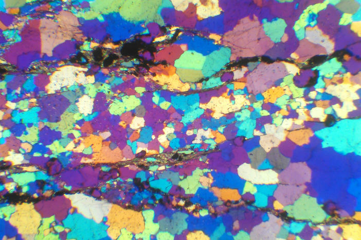 A thin, polished slice of a rock collected from the Jack Hills of Western Australia, viewed through a special microscope equipped with a gypsum plate that shows the rainbow spectrum of quartz that makes up the rock. Whereas the rocks at the Jack Hills are greater than 99% quartz, the remaining 1% of material includes the precious zircons.