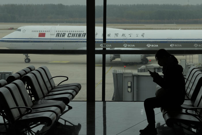 A passenger checks her phone as an Air China passenger jet taxis past at the Beijing Capital International airport on Oct. 29. China will drop a COVID-19 quarantine requirement for passengers arriving from abroad starting Jan. 8.