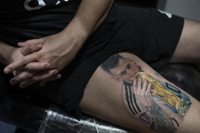 Sebastian Fernandez rests as artist César "Yeyo" Molina tattoos his leg with an image of soccer player Lionel Messi kissing the World Cup trophy, in Buenos Aires, Argentina, Thursday, Dec. 29, 2022.
