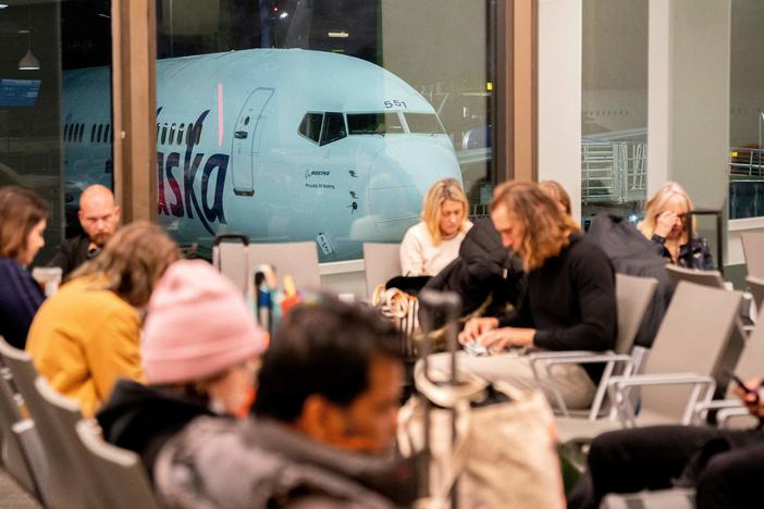 Travelers wait in the terminal as an Alaska Airlines plane sits at a gate at Los Angeles International Airport early Wednesday.