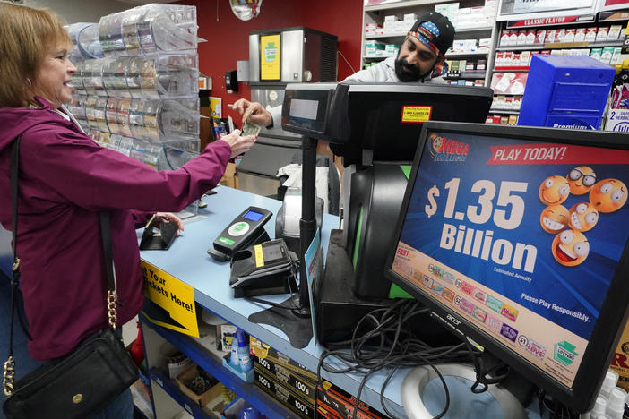 A Mega Millions sign displays the estimated jackpot of $1.35 billion as a customer purchases a ticket at the Cranberry Super Mini Mart in Cranberry, Pa., on Jan. 12, 2023.