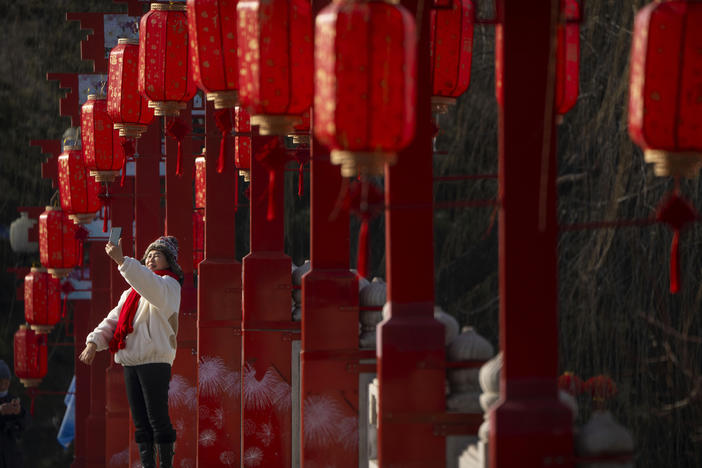 A woman poses for a selfie on a bridge decorated with lanterns at a public park in Beijing on the first day of the Lunar New Year holiday, Sunday, Jan. 22, 2023.