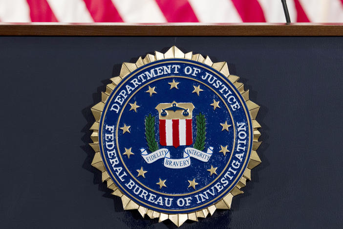 The FBI seal is displayed on a podium. A former FBI agent is facing several charges tied to his work with a Russian oligarch.