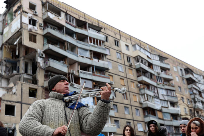 A man plays violin on the sidelines of a religious service held by local residents in front of an apartment building in the Ukrainian city of Dnipro on Sunday. The building was destroyed by a Russian missile strike on Jan. 14.