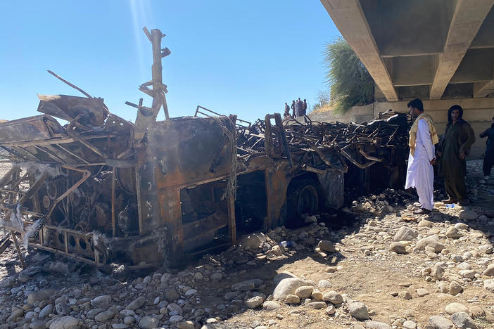 People look at the burnt wreckage of a bus in Bela, an area of Lasbela district of Balochistan province, Pakistan, on Sunday. The passenger bus crashed into a pillar and fell off a bridge, catching fire and killing dozens of people.