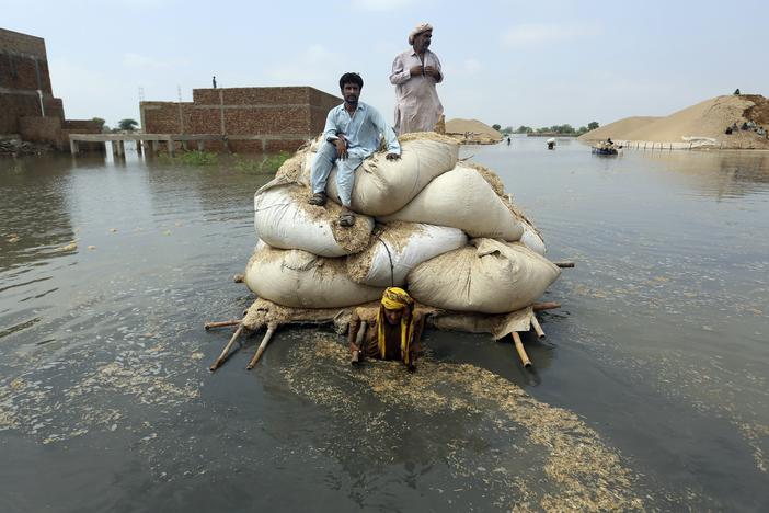 Residents of southwest Pakistan move through floodwaters in September 2022. People with less wealth are more vulnerable to the effects of climate change, including more severe rainstorms.