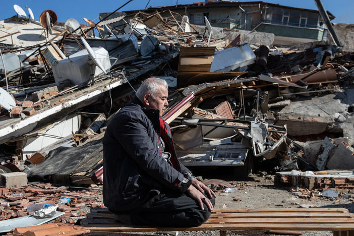 A man prays in front of a collapsed building in Hatay, Turkey.