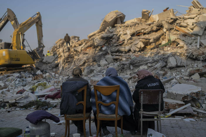 Women sit in front of the rubble of an area destroyed during the earthquake in Antakya, southeastern Turkey, Sunday, Feb. 12, 2023.