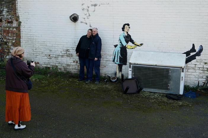People gathered to see a Banksy artwork on the side of a house in Margate, England, on Valentine's Day. The work depicts a 1950s housewife with a swollen eye, missing a tooth — and apparently shutting a man in a freezer. The freezer was later removed by council workers.