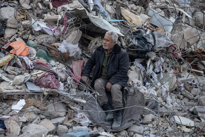 A man watches a search and rescue operation from a pile of rubble in Hatay, Turkey, after the earthquake.