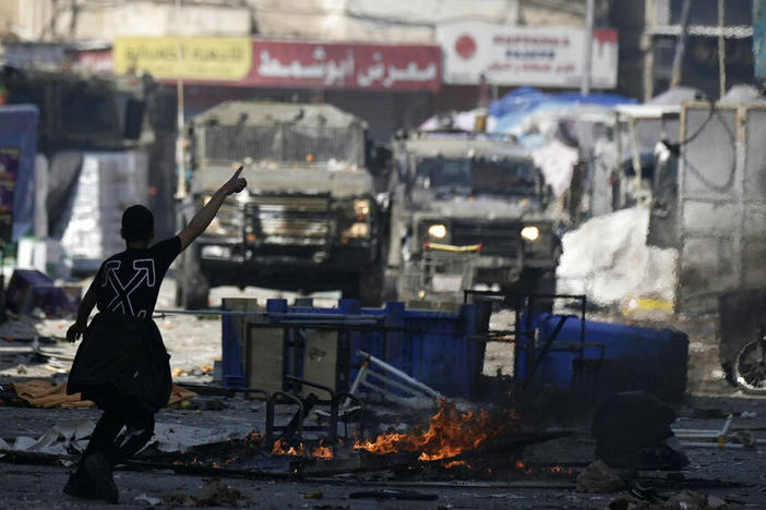 A Palestinian gestures to Israeli military vehicles Wednesday during clashes in the West Bank city of Nablus.