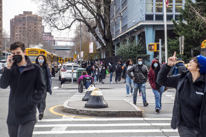 Pedestrians cross Houston Street as students wearing masks leave the New Explorations into Science, Technology and Math (NEST+m) school in the Lower East Side neighborhood of Manhattan on Tuesday, Dec. 21, 2021, in New York.