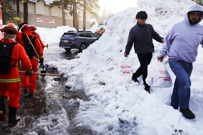 A crew of inmate firefighters walk back to their vehicle after shoveling and clearing snow, while people carry bags of food on Friday. A series of winter storms in the San Bernardino Mountains in Southern California left residents stranded due to the snowfall.