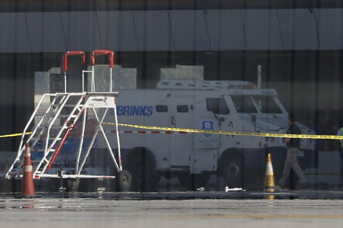 Photographed through a fence, an armored truck is surrounded by police tape at the Arturo Merino Benitez International Airport in Santiago, Chile, on Wednesday. An airport shootout killed a security officer and an alleged robber in what authorities say was an attempted heist of more than $32 million in cash aboard a plane from Miami.