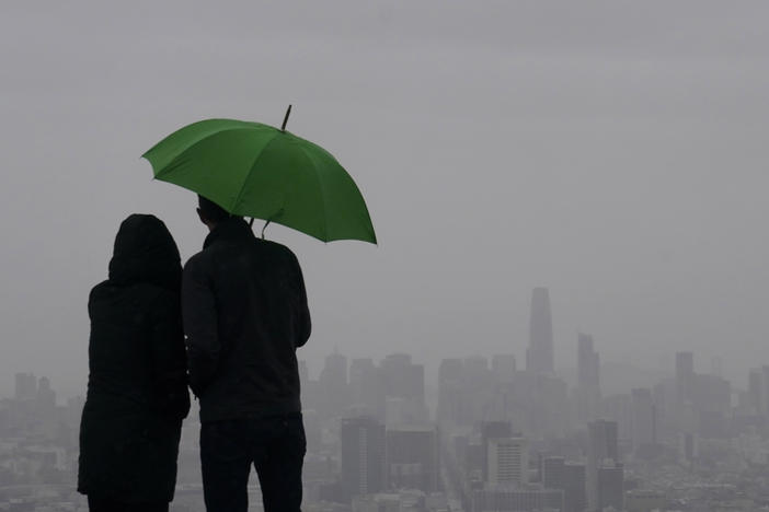 People stand under an umbrella while looking toward the skyline from Twin Peaks in San Francisco, Thursday, March 9, 2023.