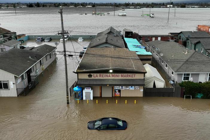 This aerial photograph shows a car and market shop in floodwaters in Pajaro, Calif., on Saturday. More rain and snow is expected in the state this week.