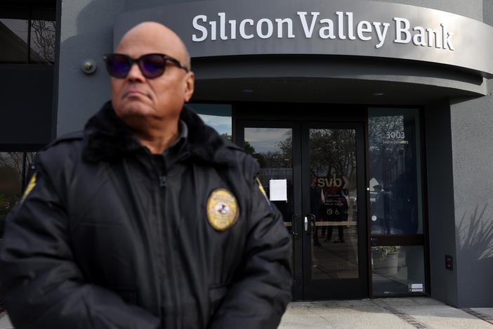 A security guard at Silicon Valley Bank monitors a line of people outside the office in Santa Clara, Calif., on March 13, 2023. The Fed will now need to factor in the impact of the collapse of the lender, along with Signature Bank, as it makes its next decision on interest rates.