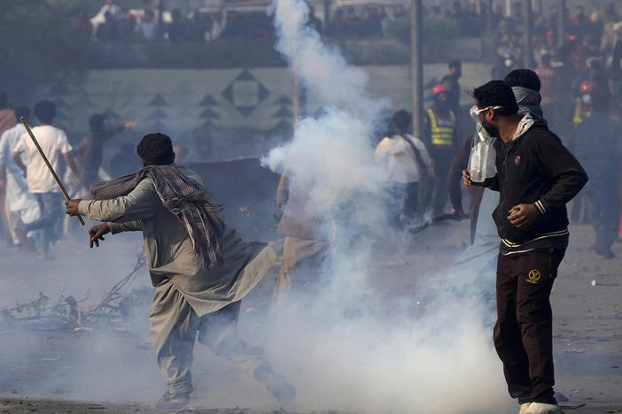 A supporter of former Prime Minister Imran Khan hurls back a tear gas shell fired by riot police officers to disperse them during clashes, in Lahore, Pakistan, Wednesday, March 15, 2023.