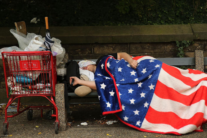 An unhoused individual sleeps under an American flag blanket in New York City on Sept. 10, 2013. In 2021, approximately 11% of Americans lived below the federal poverty line.