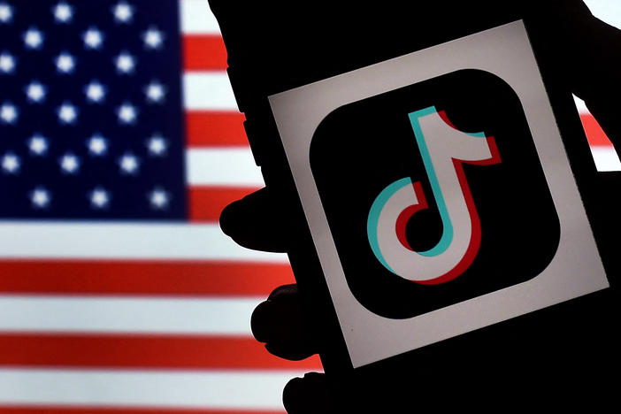 The social media application logo, TikTok is displayed on the screen of an iPhone on an American flag background. With the TikTok CEO set to testify on Capitol Hill on Thursday, influencers and lobbyists are pressing the government not to ban the app.