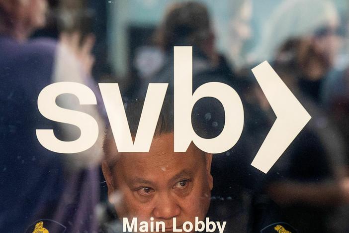 A security guard looks out a door as customers line up at Silicon Valley Bank headquarters in Santa Clara, California on March 13, 2023.