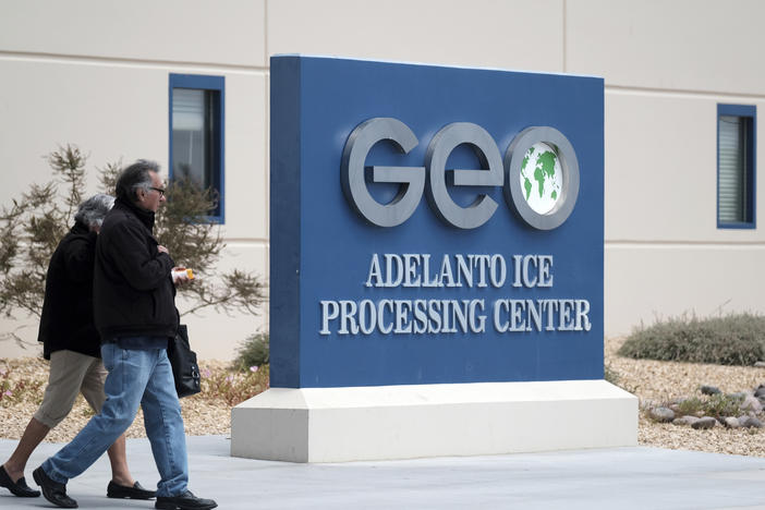 People walk outside the U.S. Immigration and Enforcement Processing Center operated by GEO Group Inc. in Adelanto, Calif. The company is facing a lawsuit for the alleged use of hazardous chemicals in the facility during the COVID-19 pandemic.