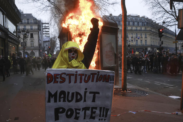 A protester holds a placard that reads, "destitution of the cursed poet " during a rally in Paris on Thursday. French unions held their first mass demonstrations Thursday since President Emmanuel Macron enflamed public anger by forcing a higher retirement age through parliament without a vote.