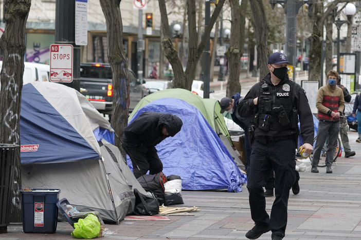 A Seattle police officer walks past tents used by people experiencing homelessness, March 11, 2022, during the clearing and removal an encampment in Westlake Park in downtown Seattle.