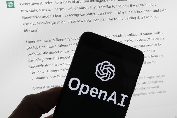 The OpenAI logo is seen on a mobile phone in front of a computer screen displaying output from ChatGPT on March 21, in Boston. A group of prominent computer scientists and other tech industry notables are calling for a 6-month pause to consider the risks of powerful artificial intelligence technology.