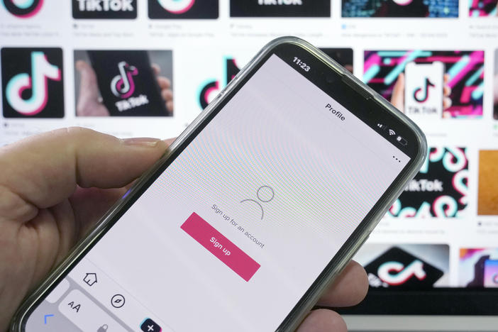 A sign up page for the application TikTok is shown on a cell phone in front of a screen with logos for the company in Sydney, Tuesday, April 4, 2023.