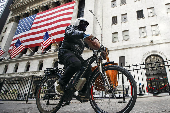 A delivery worker rides his electric bicycle past the New York Stock Exchange on March 16, 2020, in New York. Electric bicycles and scooters are being blamed in an increasing number of fires resulting in injuries and deaths in New York City.