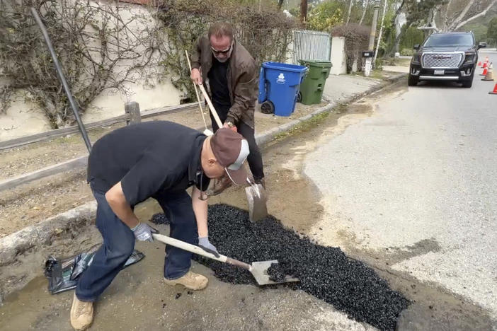 This video still image provided by Arnold Schwarzenegger's office, shows the former California governor (center back) repairing a pothole on a street in his Los Angeles neighborhood on Tuesday.