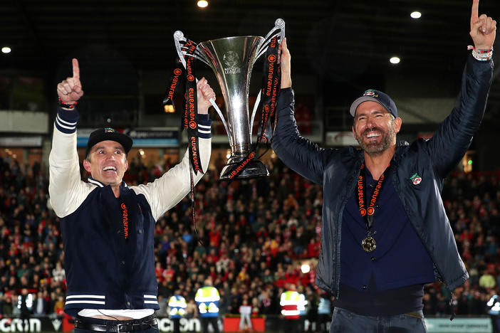 Wrexham owners Rob McElhenney and Ryan Reynolds celebrate with the Vanarama National League trophy after Wrexham won the Vanarama National League on Saturday at Racecourse Ground in Wrexham, Wales.