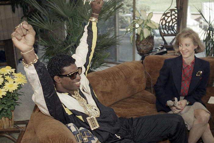 Deion Sanders, left, reacts as he sits with television reporter Andrea Kremer, at his agent's suburban home in Winnetka, Ill., April 23, 1989. Sanders was selected by the Atlanta Falcons in the first round of the NFL draft. Sanders became the NFL draft's first fashion icon by accessorizing a black and white track suit with a loads of sparkling gold jewelry and dark shades.