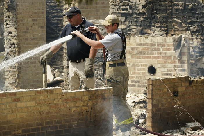 A member of the Mississippi State Fire Marshal's Office, left, waits as a firefighter waters down a burned out house, Wednesday, April 26, 2023, in Conway, Miss. Authorities believe a man who escaped from a Mississippi jail over the weekend with three others is believed to be dead in the house after a shootout with authorities and barricaded himself inside a burning home near Conway.