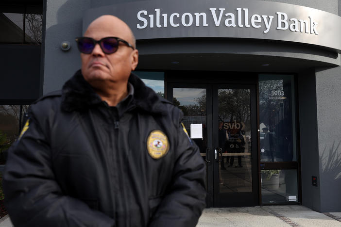 A security guard at Silicon Valley Bank monitors a line of people outside the office in Santa Clara, Calif., on March 13, 2023. The Fed admitted it was partly to blame for the collapse of the lender in a scathing report on Friday.