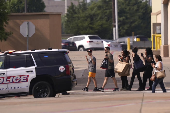People raise their hands as they leave a shopping center following reports of a shooting, in Allen, Texas, on Saturday.