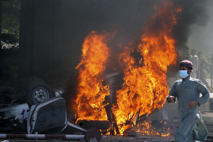 A man runs past a burning car set on fire by angry supporters of Pakistan's former Prime Minister Imran Khan during a protest against the arrest of their leader, in Peshawar, Pakistan, Wednesday. A court has ruled that former Pakistani Prime Minister Imran Khan can be held for questioning for eight days. His detention set off clashes between his supporters and police Tuesday.