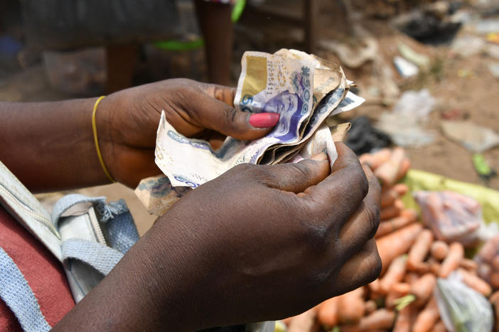 A vendor in a market in Nigeria counts local bills. The country is one of dozens whose devalued currency is fueling a debt crisis.