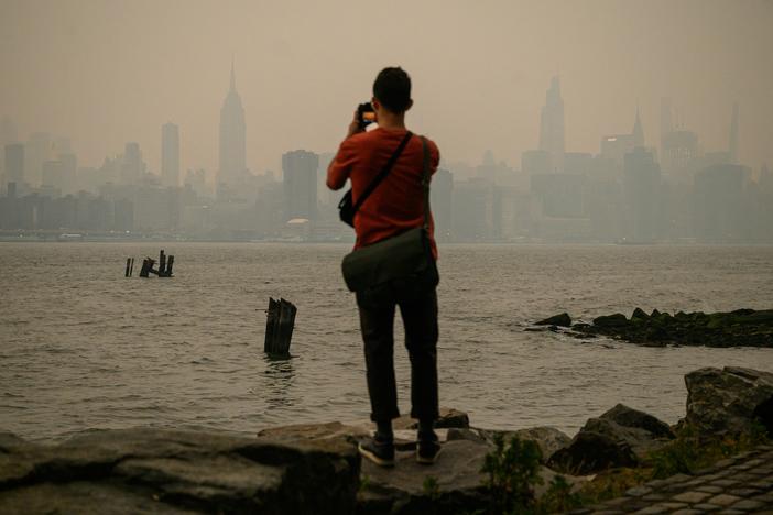 A man stands before the smoky New York City skyline and East River in Brooklyn on Tuesday.