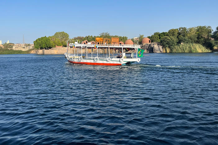 A small motorboat cruises down the Nile River in Aswan, Egypt, past domed Nubian structures.