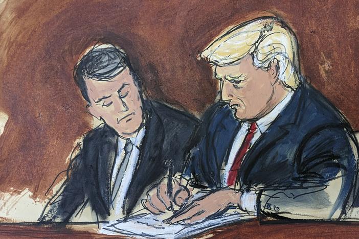 Former President Donald Trump, center, flanked by his defense attorneys, signs his bond in federal court on Tuesday in Miami. Trump plead not guilty to federal charges that he illegally kept classified documents at his Florida estate.