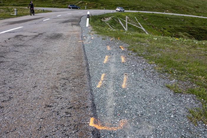 Paint outlines of what look to be two tire tracks leading off the road at the curve where Swiss rider Gino Mäder fell during a high-speed descent of the fifth stage of the Tour de Suisse. Mäder, 26, died from injuries he sustained when he plunged into a ravine.