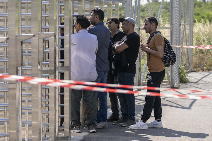 A group of men wait at the turnstiles and speak with survivors, mostly from Pakistan, of a deadly migrant boat sinking at a migrant camp in Malakasa north of Athens, on Monday, June 19, 2023.