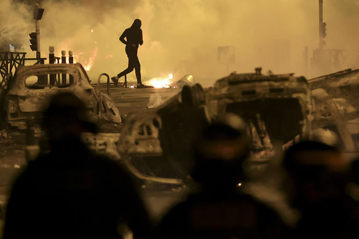A demonstrator runs on the third night of protests sparked by the fatal police shooting of a 17-year-old driver in the Paris suburb of Nanterre, France, Friday, June 30, 2023.