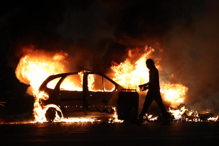 A man walks by a burning car during clashes with police in Le Port on the French Indian Ocean island of La Reunion, on Friday over the fatal shooting by police of a 17-year-old in a Paris suburb.