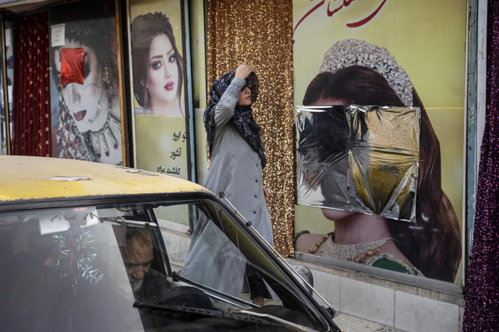 A woman walks past beauty salons with window decorations that have been defaced in Kabul, Afghanistan, Sunday, Sept. 12, 2021.