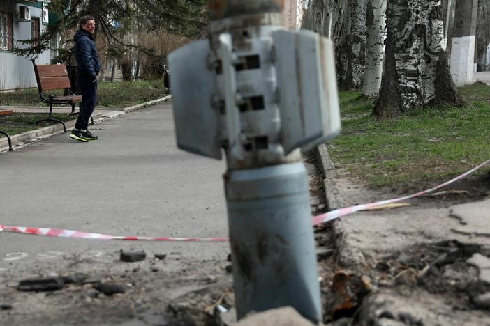 A man walks past an unexploded tail section of a 300mm rocket which appear to contained cluster bombs launched from a BM-30 Smerch multiple rocket launcher embedded in the ground after shelling in Lysychansk, Lugansk region on April 11, 2022.