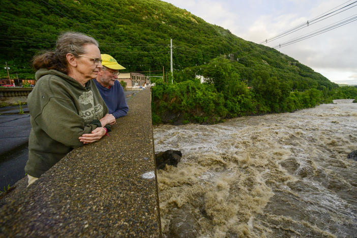 People stand on the Vilas Bridge, in Bellows Falls, Rockingham, Vt., to watch the water from the Connecticut River flow through on Monday, July 10, 2023. Heavy rain has washed out roads and forced evacuations in the Northeast, especially in Vermont and New York.