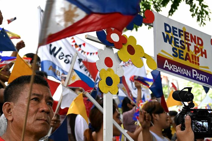 Protesters wave flags and hold placards in front of the Chinese Consulate in Makati, Metro Manila on July 12, 2023, during a demonstration held to mark the seventh anniversary of an international arbitral ruling that voided China's historical claims to the South China Sea, including the nine-dash line.